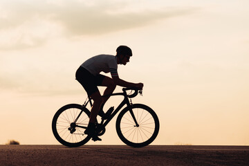 Fototapeta na wymiar Silhouette of man in helmet riding bike during sunset