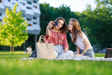 Two girls are sitting in the park, laughing and joking, taking a selfie in the courtyard of the college