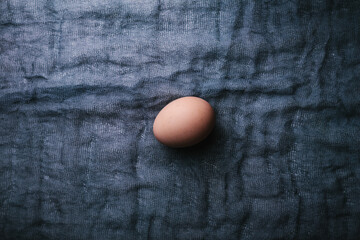 One egg on dark fabric background. Easter, spring or eco food concept. Top View