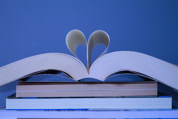 group of books and above one open in the middle with two pages forming a heart for the reading on...