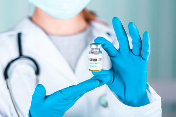 Obraz premium Doctor or nurse in uniform and gloves wearing face mask protective in lab holding medicine vial vaccine bottle with COVID-19 Coronovirus vaccine label