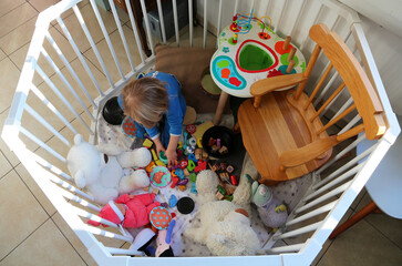 little girl playing with all her toys in babypen