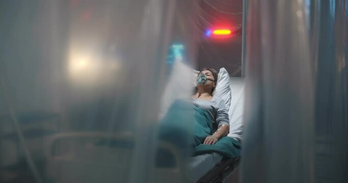 Sick aged woman with oxygen mask coughing lying in quarantine ward at hospital