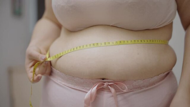 Woman suffering from abdominal fat measuring waistline by tape, progress of diet