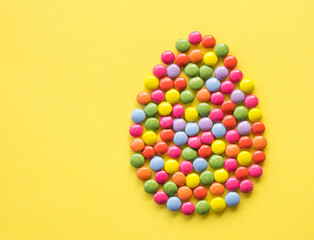 Easter egg from colorful chocolate candies on the yellow background with copy space