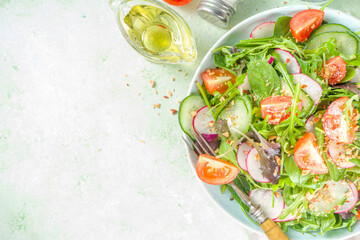 Fresh colorful spring salad with tomatoes, avocado, walnuts, cucumber, spring radish, on light green background copy space. Spring diet healthy food concept