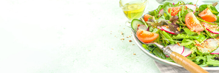 Fresh colorful spring salad with tomatoes, avocado, walnuts, cucumber, spring radish, on light green background copy space. Spring diet healthy food concept