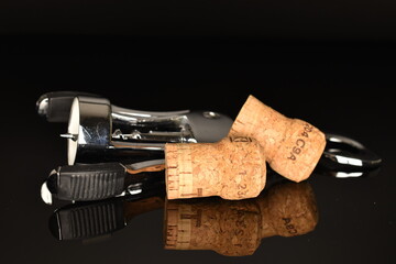Several light brown, wine corks with a wine opener, close-up on a black background.