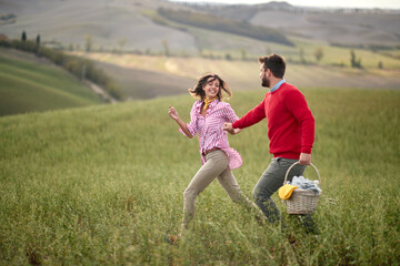 Obraz premium A young happy couple enjoying the nature and a large meadow while looking for a picnic spot. Love, relationship, together, nature