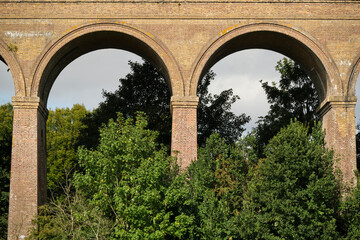 Arches of Chappel Viaduct in Essex, England. Pillars and arches of railroad bridge Chappel Viaduct in rural Essex, England with green trees against blue skies on sunny day.