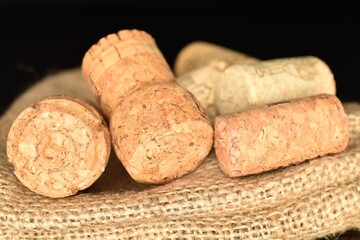 Several wine corks, close-up, on a jute napkin, on a black background.