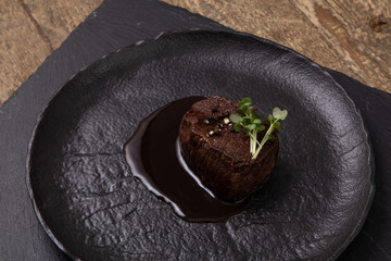 Cooked beef chop with gravy and micro greens on a black plate