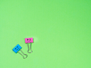 Funny blue and pink smile metal binder clip or multicolored paperclip on green background with copyspace for text