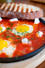 Shakshuka (shakshouka), Jewish national fried eggs, with cheese, herbs and tomatoes, on a board, with toasted toast, close, with a blur