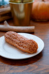 Long chocolate eclair with sprinkles on a white plate, close, with a blur