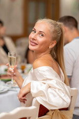 beautiful blonde in a white outfit sits in a restaurant with a glass of champagne.