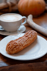 long chocolate eclair with sprinkles on a white plate with a cup of coffee, close, with a blur