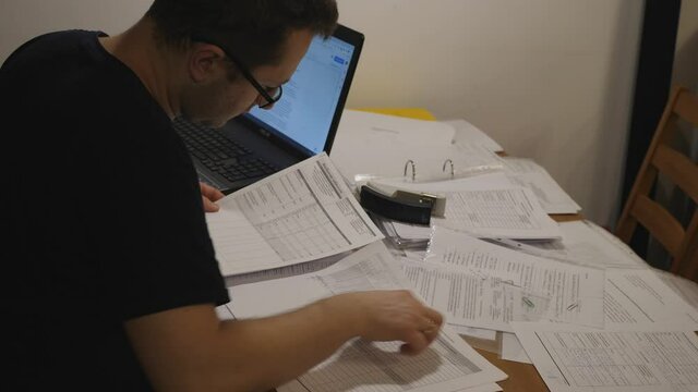 young man working studying at night at his desk, stack of papers