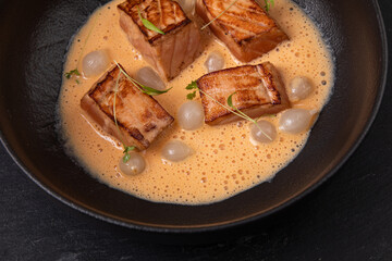 Cooked salmon peaces in creamy sauce decorated with micro greens