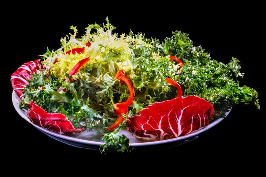 White plate with fresh green frisse salad and radiccio leaves and red pepper&rsquo;s stripes