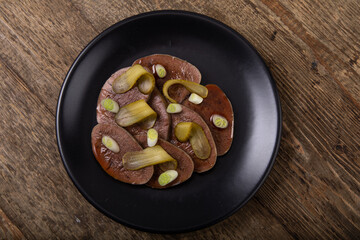 Sliced cooked cows tongue with pickled cucumbers on black plate
