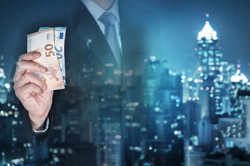 Double exposure of businessman hold EURO (EUR) money and night city as business, trade, currency, investment and income concept