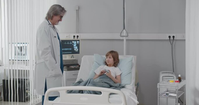 Doctor visiting child patient and shaking hands in hospital ward