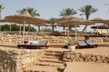 Scenic sunny landscape. Luxury beach with deck chair in the evening time. Beautiful view of Red Sea coast. Comfortable beach with lounge chairs under natural wooden umbrella