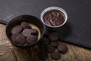 Melted milk chocolate in foil pot and chocolate buttons in a bowl