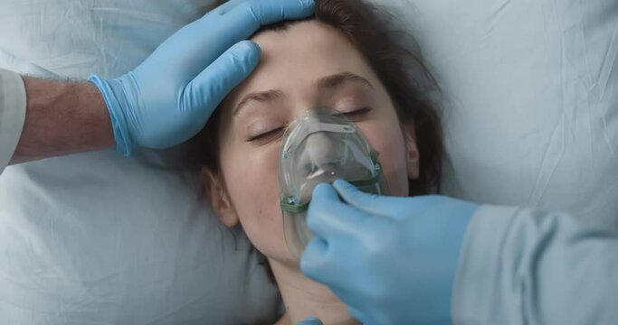 Close up of doctor in protective gloves putting oxygen mask on sick young woman