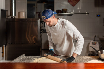 pizza boy kneads pizza dough in a pizzeria restaurant kitchen