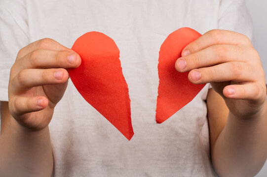 Blurred image of paper torn heart in hands on light background.
