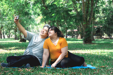 Asian fat couple, husband and attractive wife, Spent happy together, relaxing in the green garden, And using mobile phone to take a photo, concept to couple on vacation with nature.