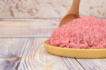 A slide of minced meat in a wooden plate. A wooden spoon is stuck in the minced meat. The plate stands on a wooden table.