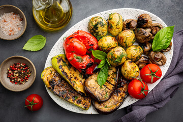 Grilled vegetables and mushrooms on plate over dark background, top view