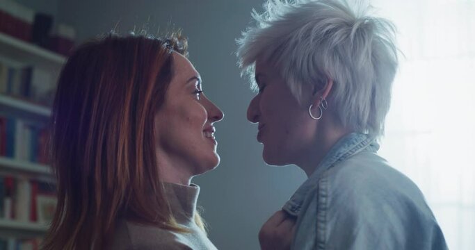 Cinematic shot of young carefree happy smiling homosexual female gay and transgender man couple in love is enjoying time together and having fun to dance together while listening to the music at home