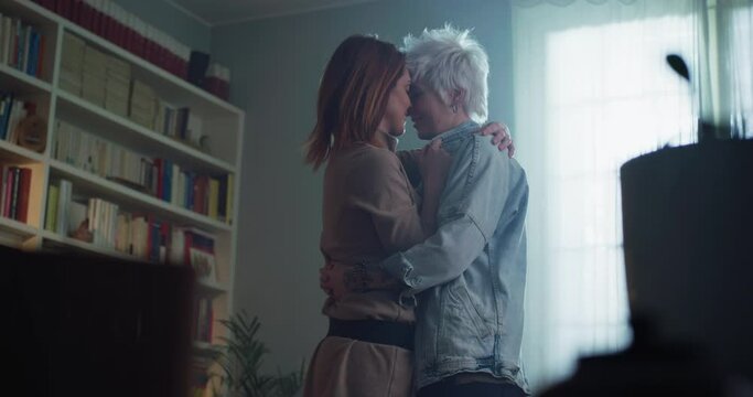Cinematic shot of young carefree happy smiling homosexual female gay and transgender man couple in love is enjoying time together and having fun to dance together while listening to the music at home