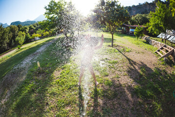 Boy splashed with water from a hose in the courtyard of the house on a hot sunny day.