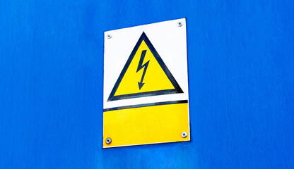 Metal plate sign with a worn yellow high voltage warning triangle symbol and an empty blank text box, blue background, copy space. Electricity, electrocution danger, hazard abstract concept, closeup