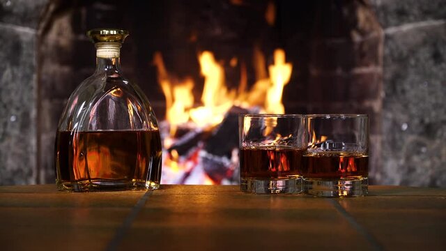 Bottle and glasses with whiskey or cognac. Burning Fire In The Fireplace. Warmth and home comfort. 4K