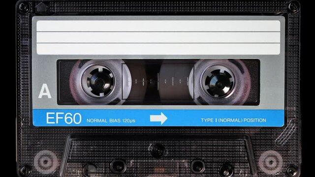 Audio cassette tape in use for sound recording in the tape recorder. A vintage white and blue, brand new blank labelled music cassette playing back in a deck player. Static video camera shot. Close up