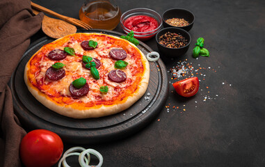 Delicious pepperoni pizza with basil, among tomatoes, onions, cheese and spices on a brown background.