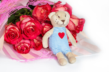 A bouquet of red roses in a gift paper package and a soft toy bear