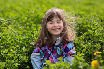 A little girl rejoices in the dense green vegetation on a sunny summer day. She laughs, her hair flutters in the wind