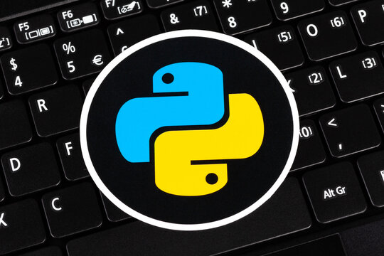 Python programming language round logo sticker, symbol label laying on a laptop keyboard, closeup, top view. Simple programming technology concept