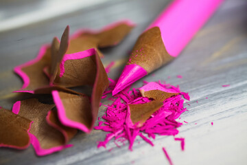 Makro closeup of isolated pink sharp crayon pencil with curly wood chips shavings on table - renewable recycable raw materials concept
