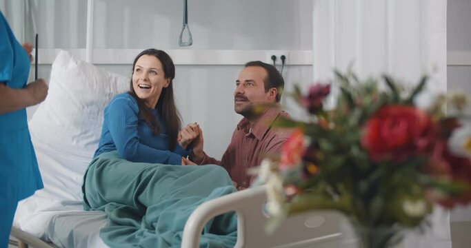 Doctor telling good news about recovery to sick woman patient and husband in hospital