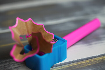 Makro closeup of isolated blue plastic pencil sharpener with pink crayon and curly wood chips shavings on table (focus on right edge of sharpener) - Powered by Adobe