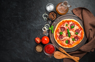 Freshly made pepperoni pizza, tomatoes, tomato sauce, onions and spices on a black background.