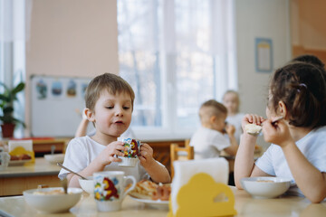 cute little boy eating cakes
 and drinking tea having breakfast in kindergarten. Image with...